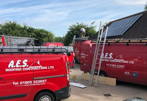 An image of two AES Roofing Contractors Ltd vans and a roofer working to create anew roof on a house.